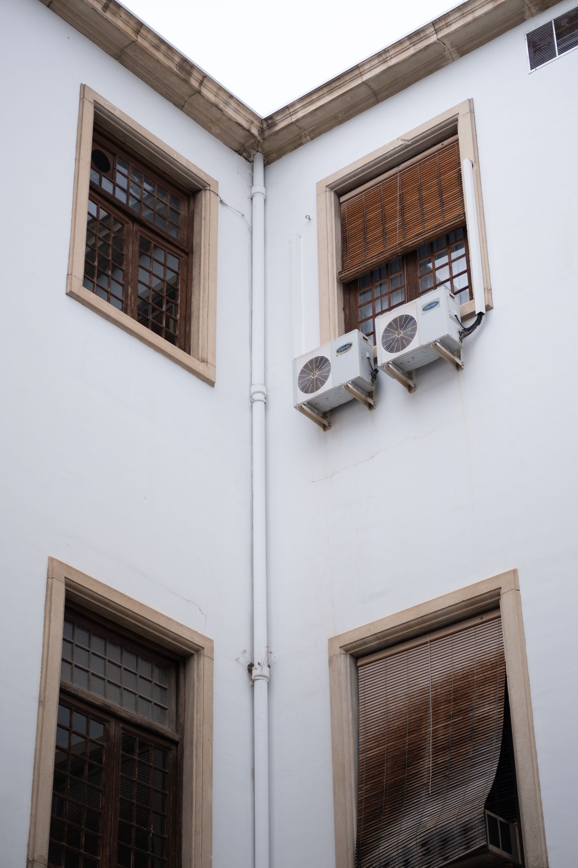 Corner of a building featuring windows with air conditioning units and wooden blinds.